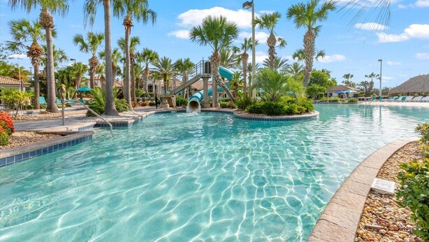 Un espace piscine avec une eau cristalline, des palmiers et un toboggan aquatique.