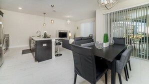 A modern kitchen with a central island, a dining area with a dark table and chairs, and a living area with a sofa and TV. - Championsgate Resort 4 Bedroom Townhome Pet Friendly 4 Townhouse (Davenport)
