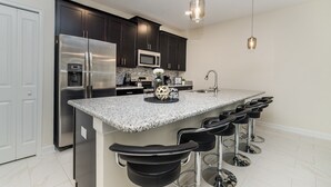 A modern kitchen with dark cabinets, stainless steel appliances, a granite countertop, and bar stools. - Championsgate Resort 4 Bedroom Townhome Pet Friendly 4 Townhouse (Davenport)