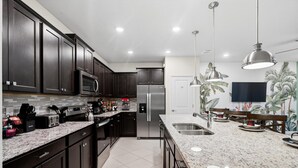 Una cucina moderna con mobili scuri, elettrodomestici in acciaio inossidabile, piani di lavoro in granito e illuminazione a sospensione.