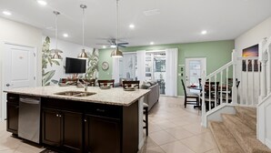 Una cucina moderna con isola centrale, illuminazione a soffitto e zona pranzo con una scala.