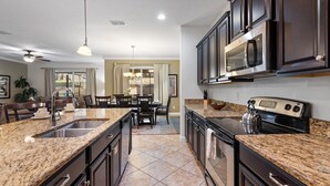 A modern kitchen with granite countertops, stainless steel appliances, and dark cabinetry. - Paradise Palms Resort 6 Bedroom Home with Game Room 6 Home (Kissimmee)