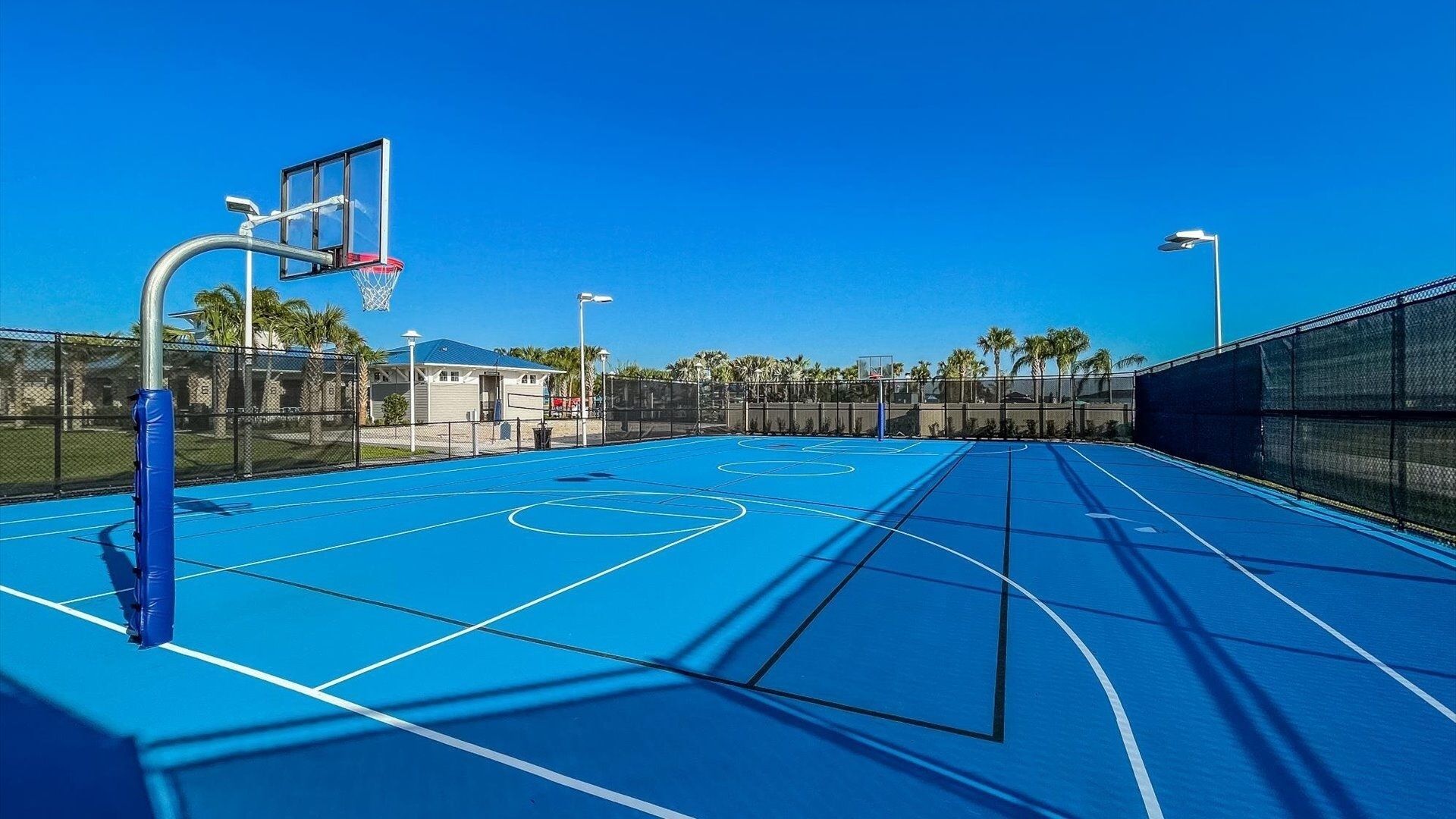 An outdoor basketball court with a blue surface, a basketball hoop, and a chain-link fence.