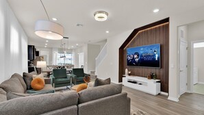 A modern living room with a sectional sofa, a flat-screen TV mounted on a wooden accent wall, and a staircase leading to another level. - Windsor Island Resort 5 Bedroom Private Pool Home 5 Home (Davenport)