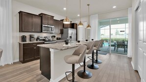 A modern kitchen with dark wood cabinets, stainless steel appliances, and a central island with bar stools. - Windsor Island Resort 5 Bedroom Private Pool Home 5 Home (Davenport)