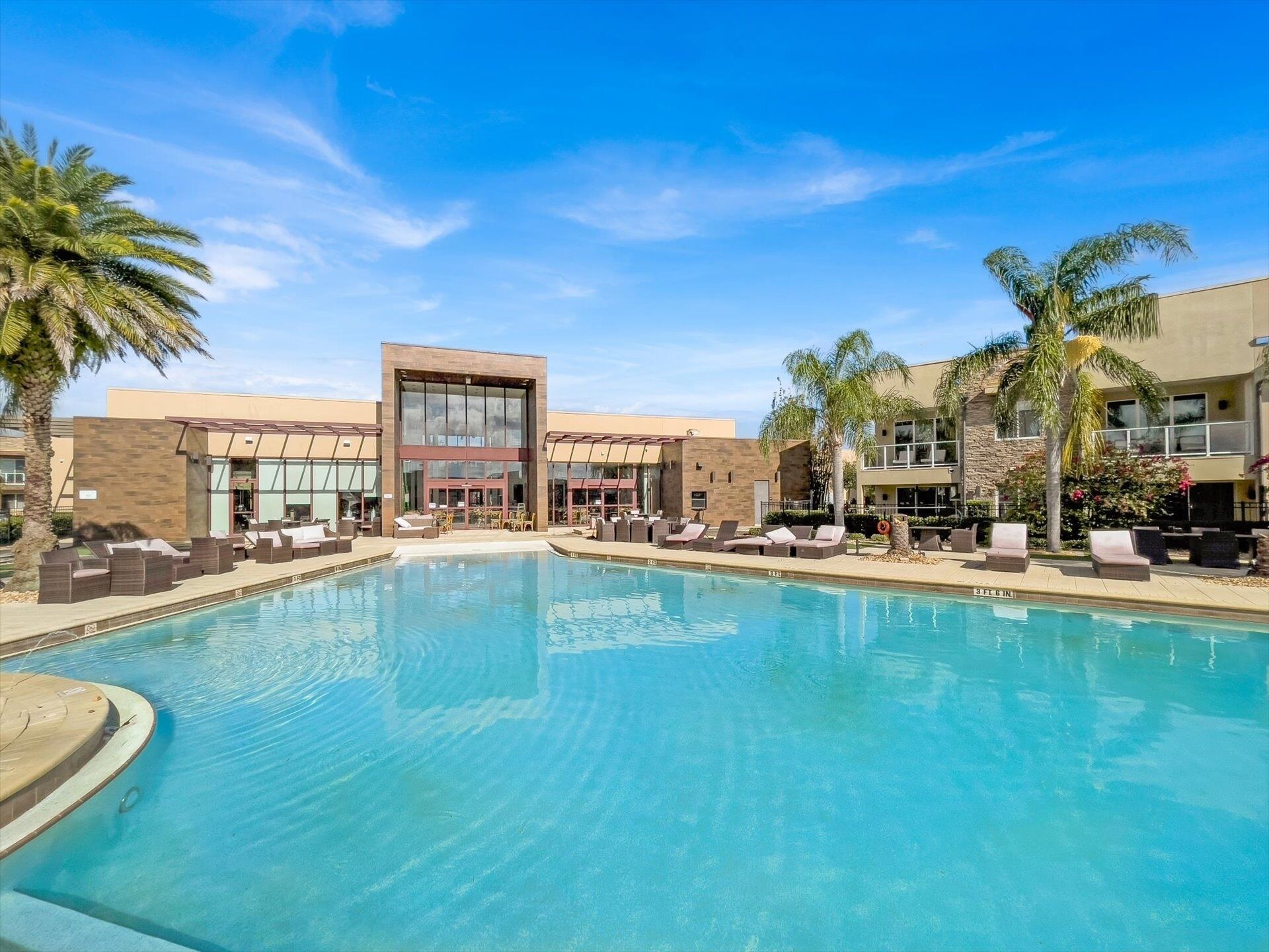 A pool area with lounge chairs and a building with large windows.