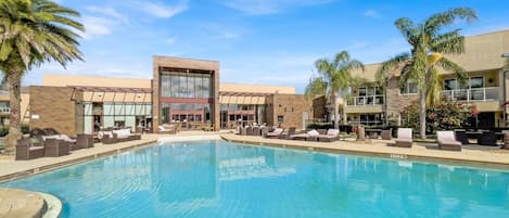A pool area with lounge chairs and a building with large windows.