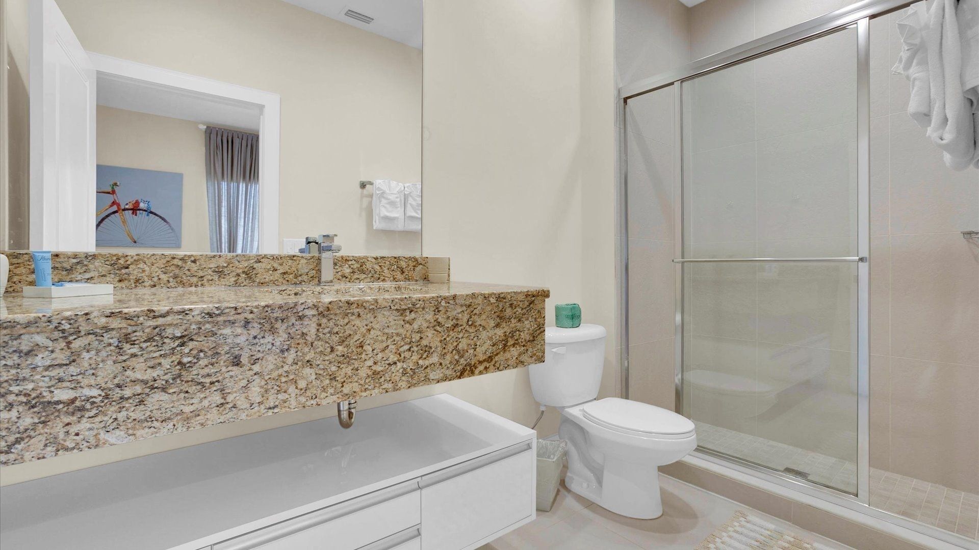 A modern bathroom with a granite countertop, a toilet, and a glass-enclosed shower.
