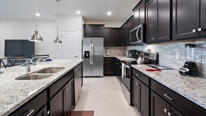 A modern kitchen with dark cabinets, granite countertops, stainless steel appliances, and pendant lighting. - Windsor Cay Resort 5 Bedroom Townhome with Pool 5 Townhouse (Clermont)