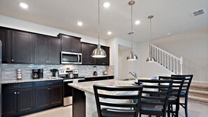 A modern kitchen with dark cabinets, a granite countertop, stainless steel appliances, and pendant lighting. - Windsor Cay Resort 5 Bedroom Townhome with Pool 5 Townhouse (Clermont)
