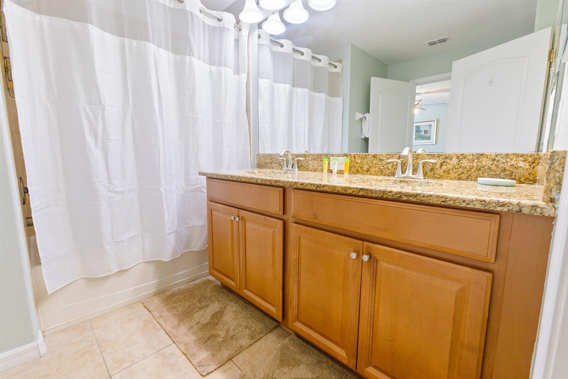 A bathroom with a wooden vanity, a granite countertop, a white shower curtain, and a mirror above the sink.