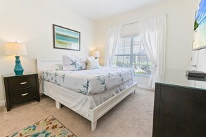Um quarto com cama, mesa de cabeceira, abajur, janela com cortinas e um quadro na parede.