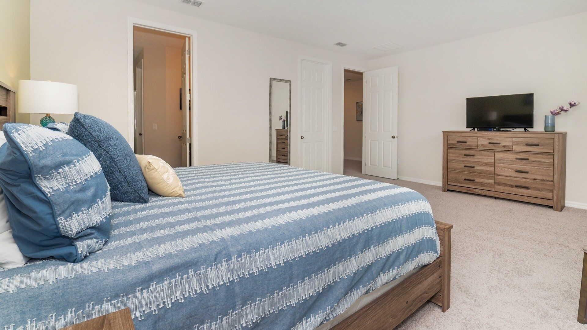A bedroom with a large bed, a dresser, a television, and two doors leading to other rooms.