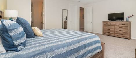 A bedroom with a large bed, a dresser, a television, and two doors leading to other rooms.