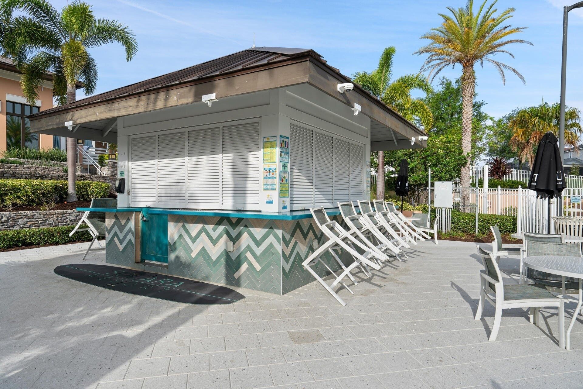 A small outdoor seating area with a sheltered table and chairs, surrounded by a stone wall and palm trees.