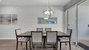 A dining area with a rectangular table, six chairs, a chandelier, and two wall-mounted paintings. - Storey Lake Resort 4 Bedroom Pet Friendly Townhome 4 Townhouse (Kissimmee)