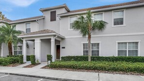 A two-story residential building with a covered entrance, a palm tree, and a well-maintained hedge. - Storey Lake Resort 4 Bedroom Pet Friendly Townhome 4 Townhouse (Kissimmee)