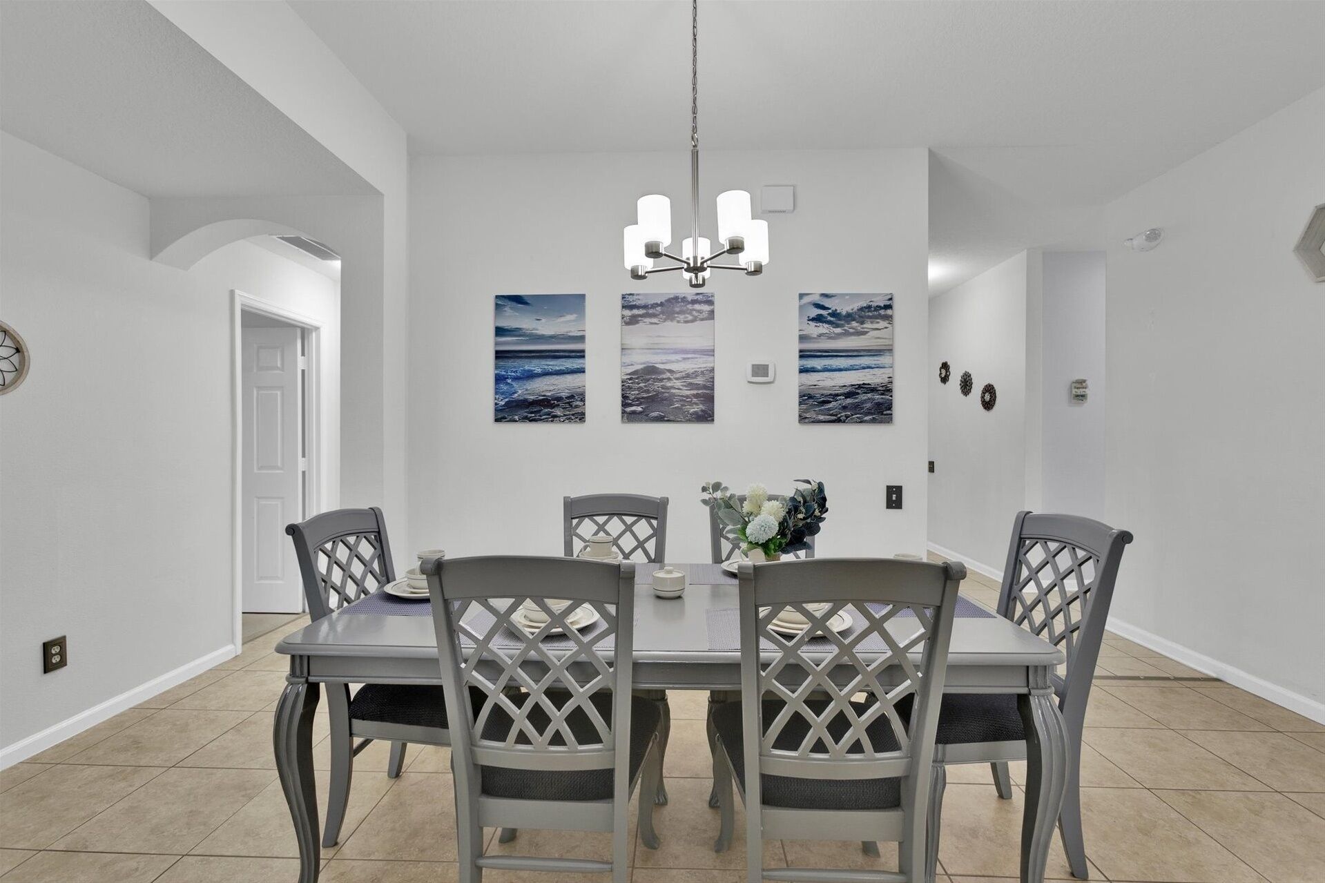Ein Essbereich mit einem runden Tisch, vier Stühlen und einer Chandelier. Über dem Tisch hängen drei gerahmte Bilder an der Wand.