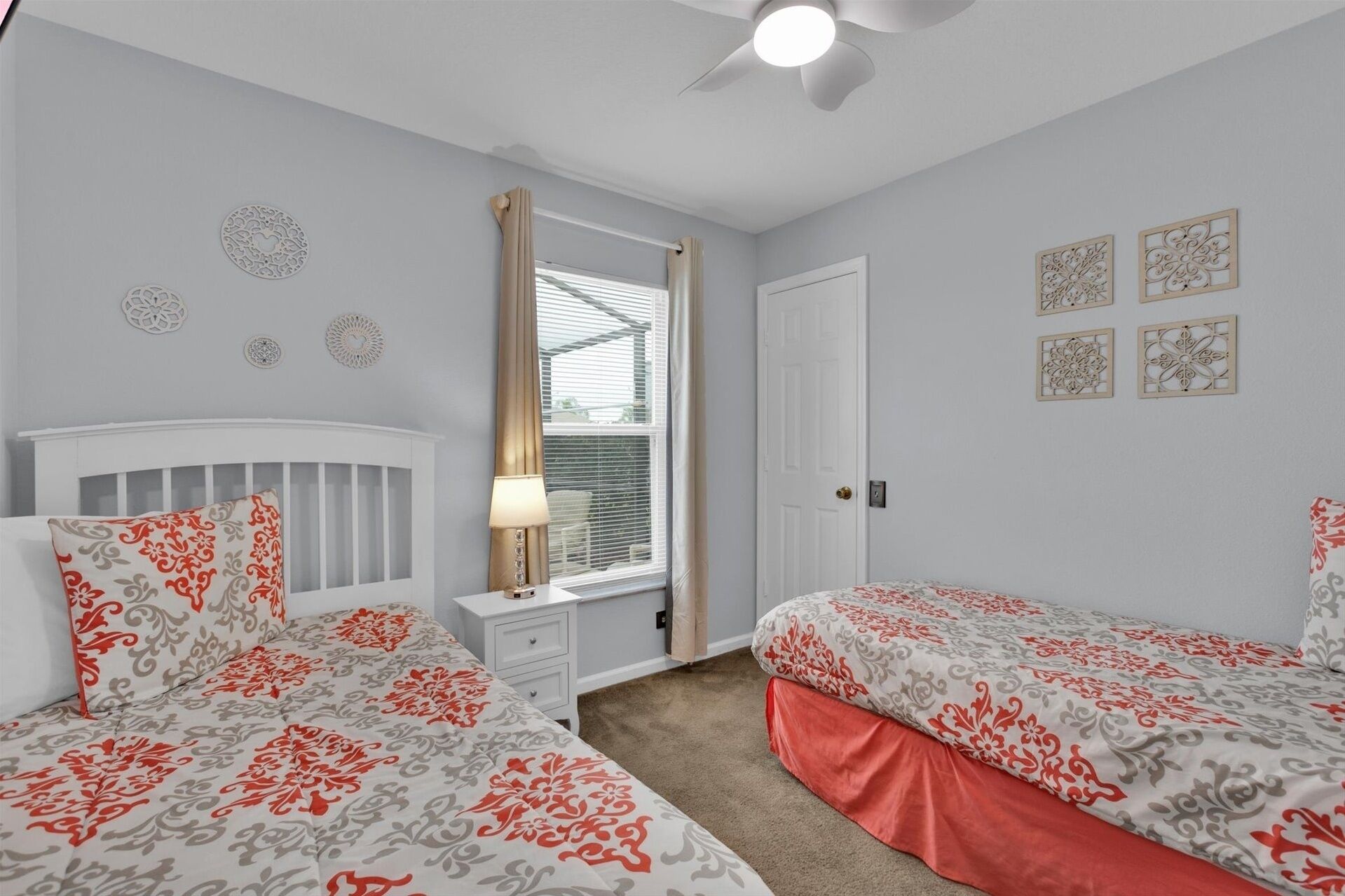 A bedroom with two beds, a window with curtains, a ceiling fan, and decorative wall art.