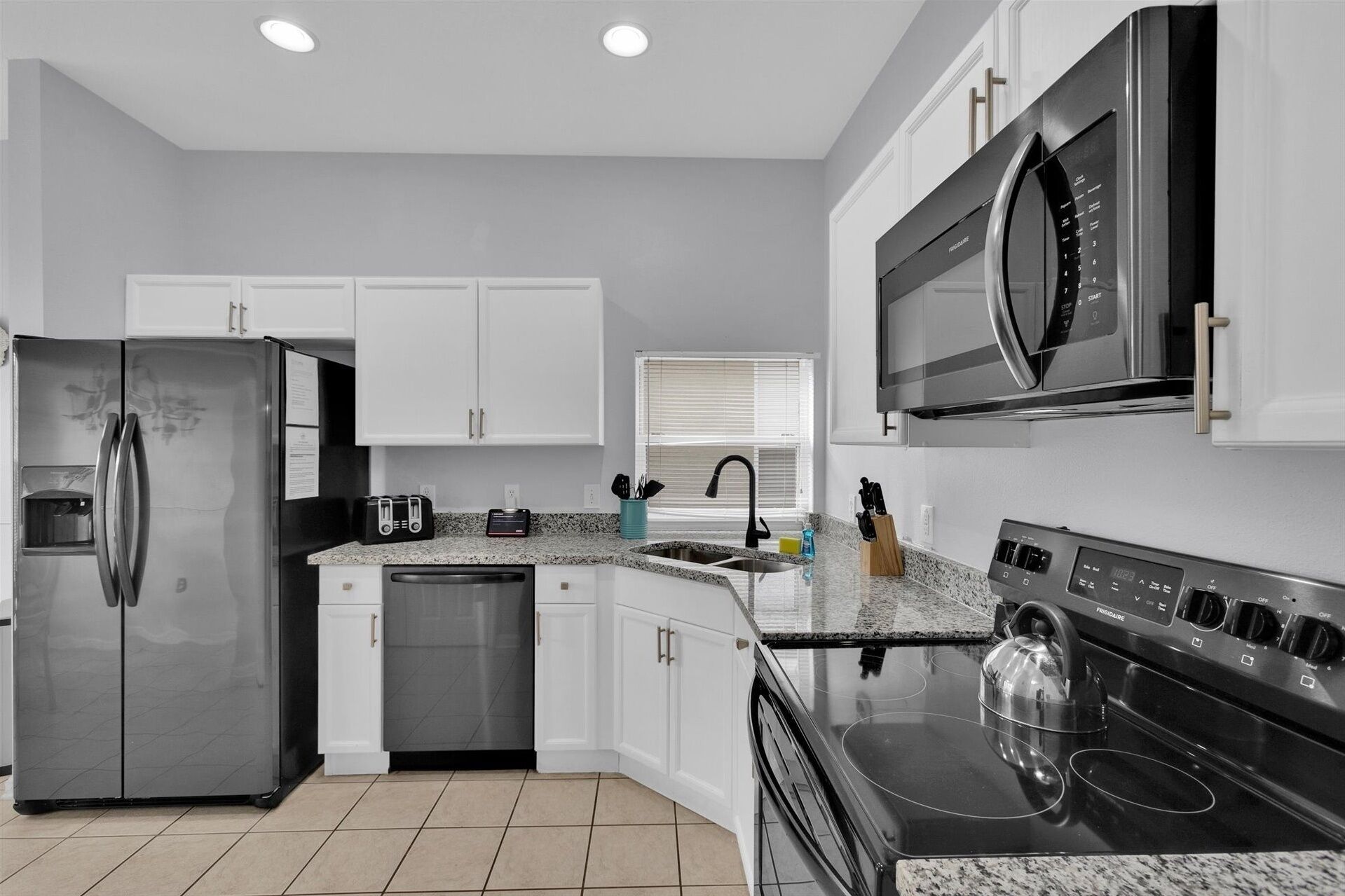 A modern kitchen with white cabinets, a stainless steel refrigerator, a built-in microwave, a dishwasher, and a stove.