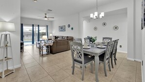 A spacious living area with a dining table set for four, a ceiling fan, and a view through glass doors to the outside. - Windsor Palms Resort 4 Bedroom with Game Room 4 Home (Kissimmee)