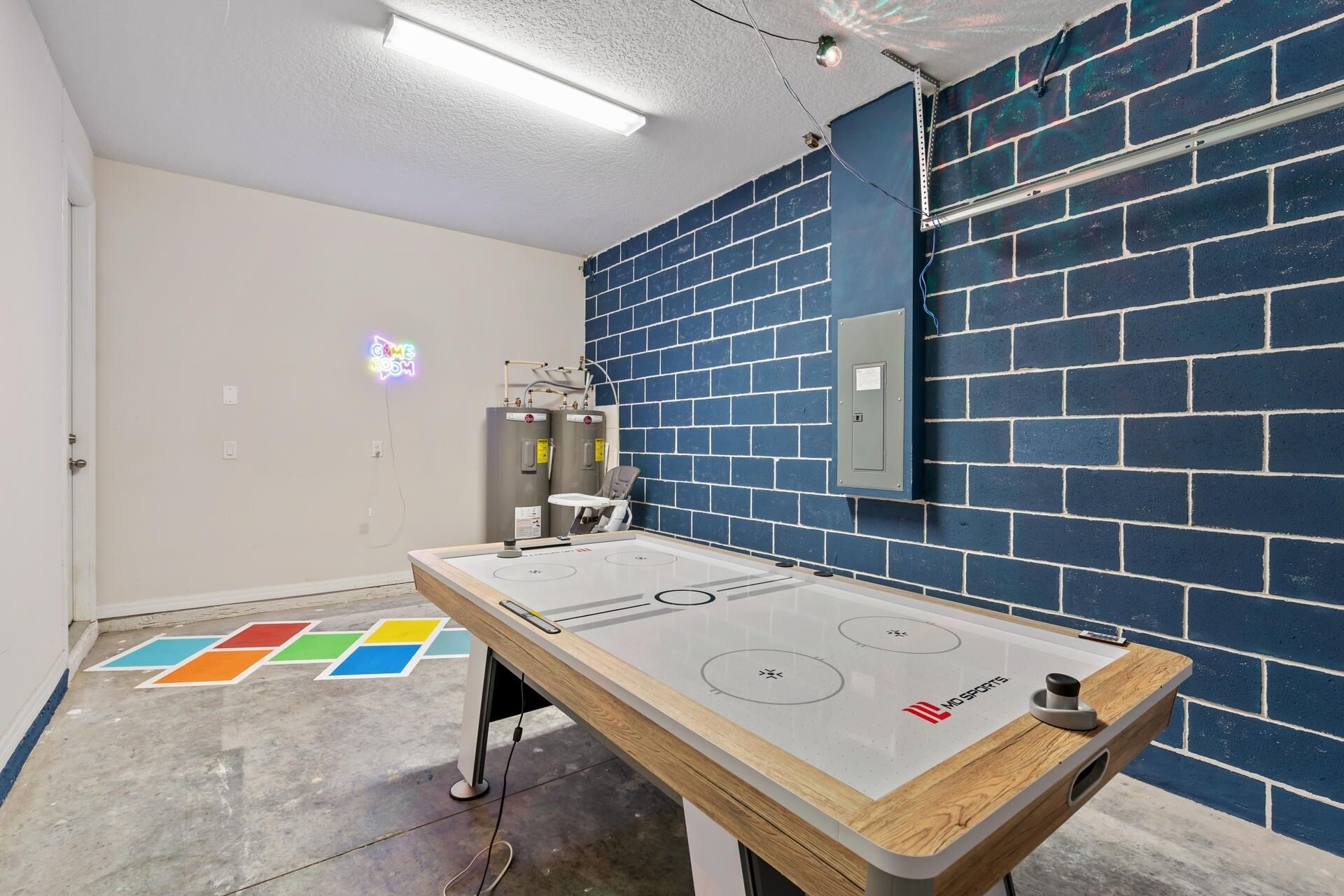 A room with a pool table, a neon sign, and a blue brick wall.