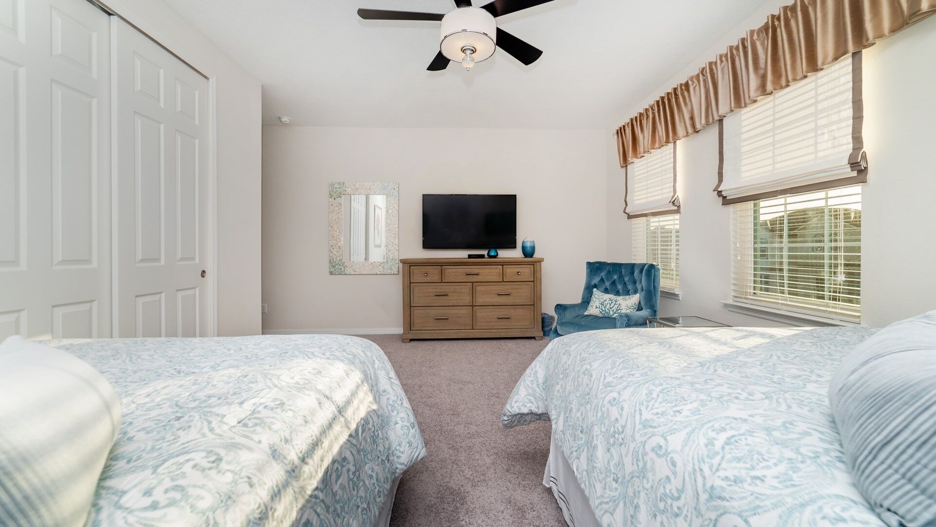 A bedroom with two beds, a dresser, a television, and a ceiling fan.
