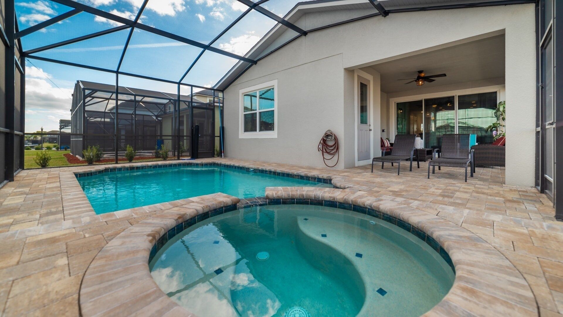 Une piscine avec un jacuzzi, entourée d’un patio couvert aménagé avec du mobilier d’extérieur.
