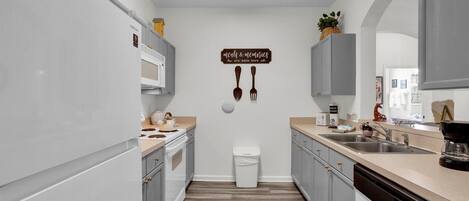 A modern kitchen with grey cabinets, a white countertop, and a wooden floor. A sign on the wall reads "meals & memories are made here."