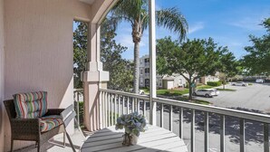 A balcony with wicker furniture, a potted plant, and a view of a residential street with houses and cars. - Windsor Palms Resort 3 Bedroom Condo with Resort Amenities 3 Condo (Kissimmee)