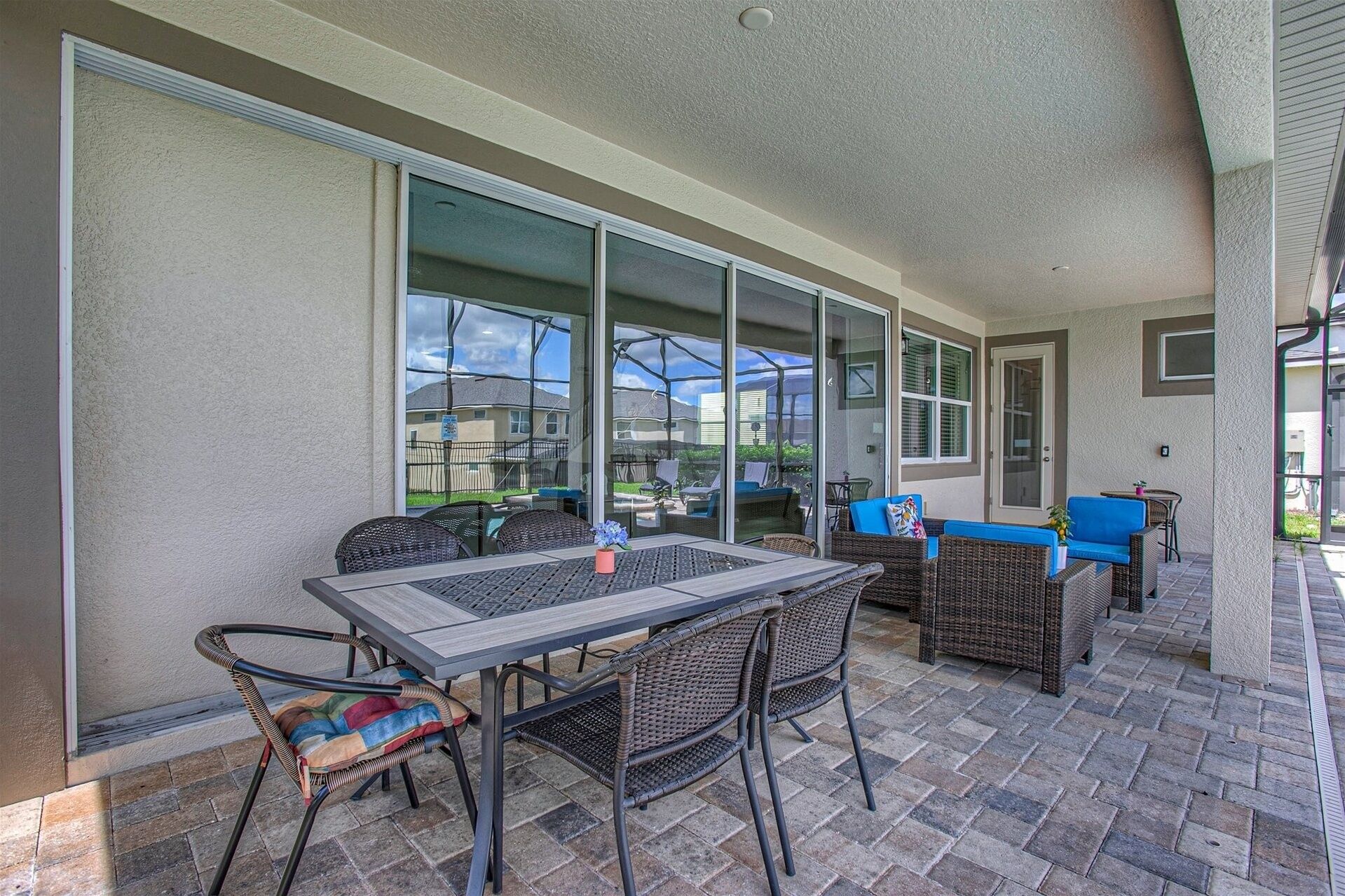 An outdoor patio with a table and chairs, large windows, and a blue sofa.