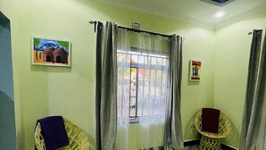A room with two wicker chairs, a large rug, and two paintings on the walls.