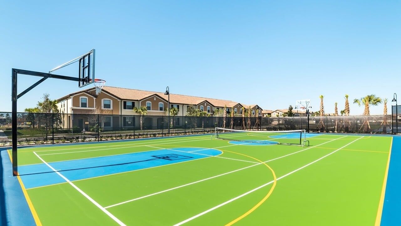 Ein Basketballplatz im Freien mit Korb, umgeben von einem Zaun und Palmen.