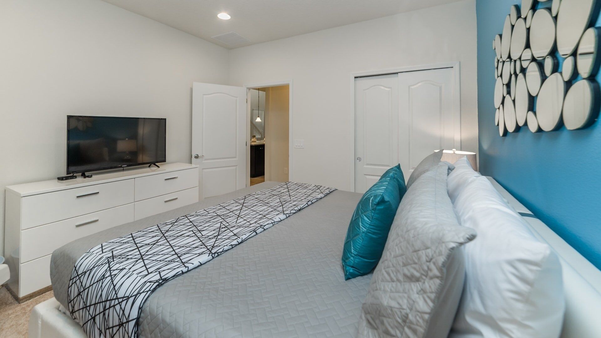 A bedroom with a bed, a TV, a wardrobe, and a door leading to another room.