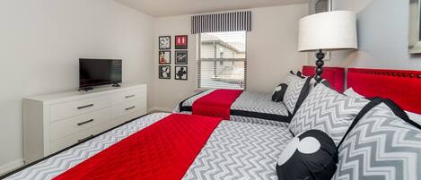 A bedroom with two beds, a TV on a white dresser, and a window with blinds.