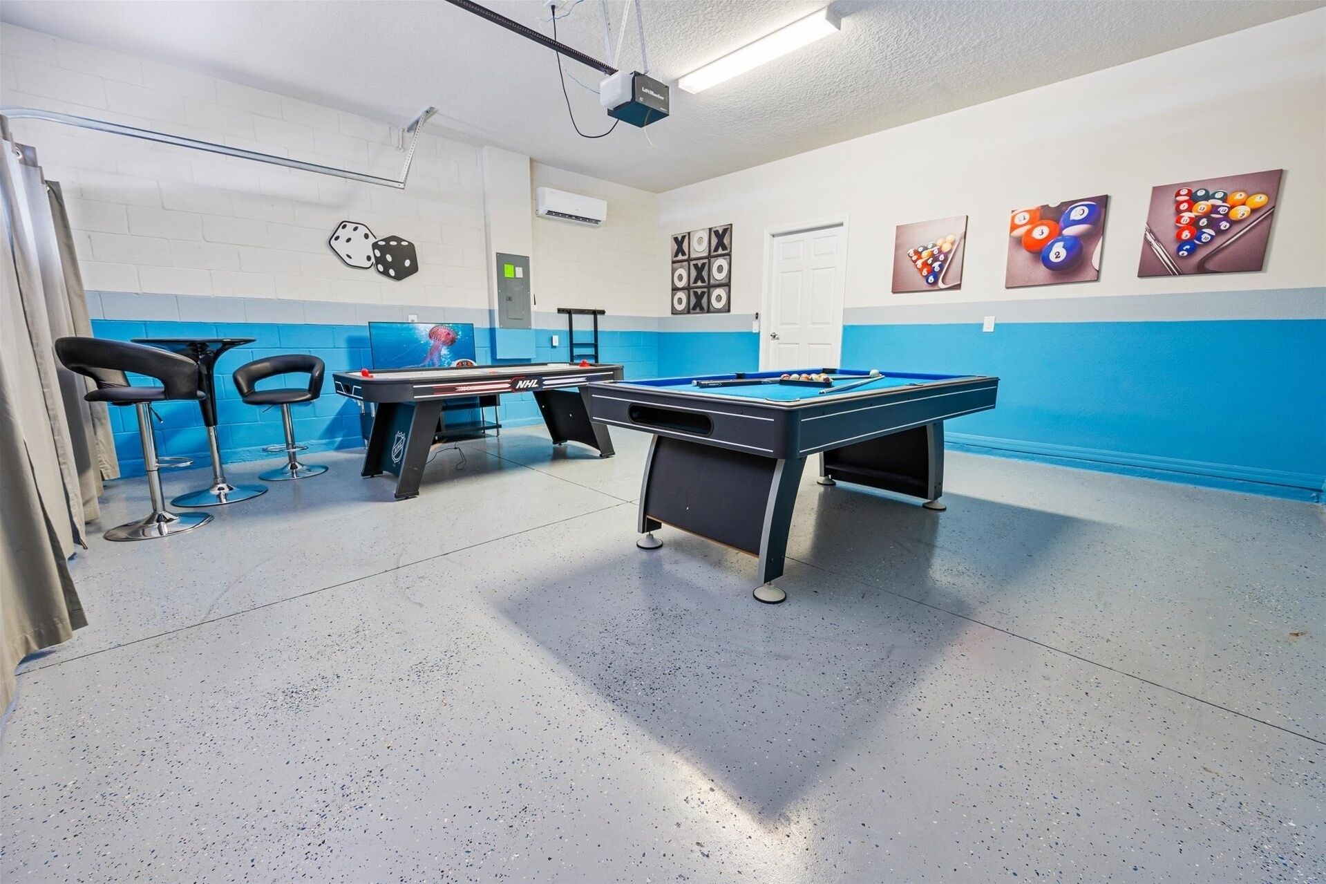 Een pooltafel in een kamer met blauwe muren, een beamer en biljartkeus aan de muur.