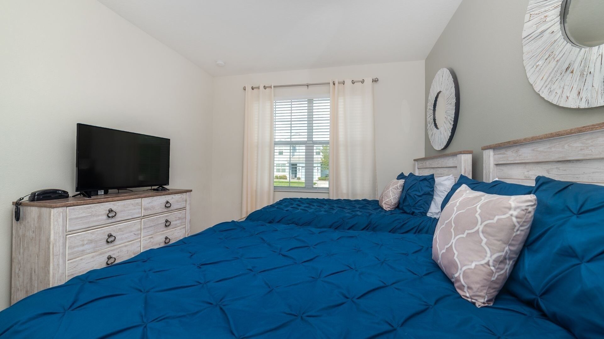A bedroom with a large bed, a TV on a dresser, and a view of the outside through a window.