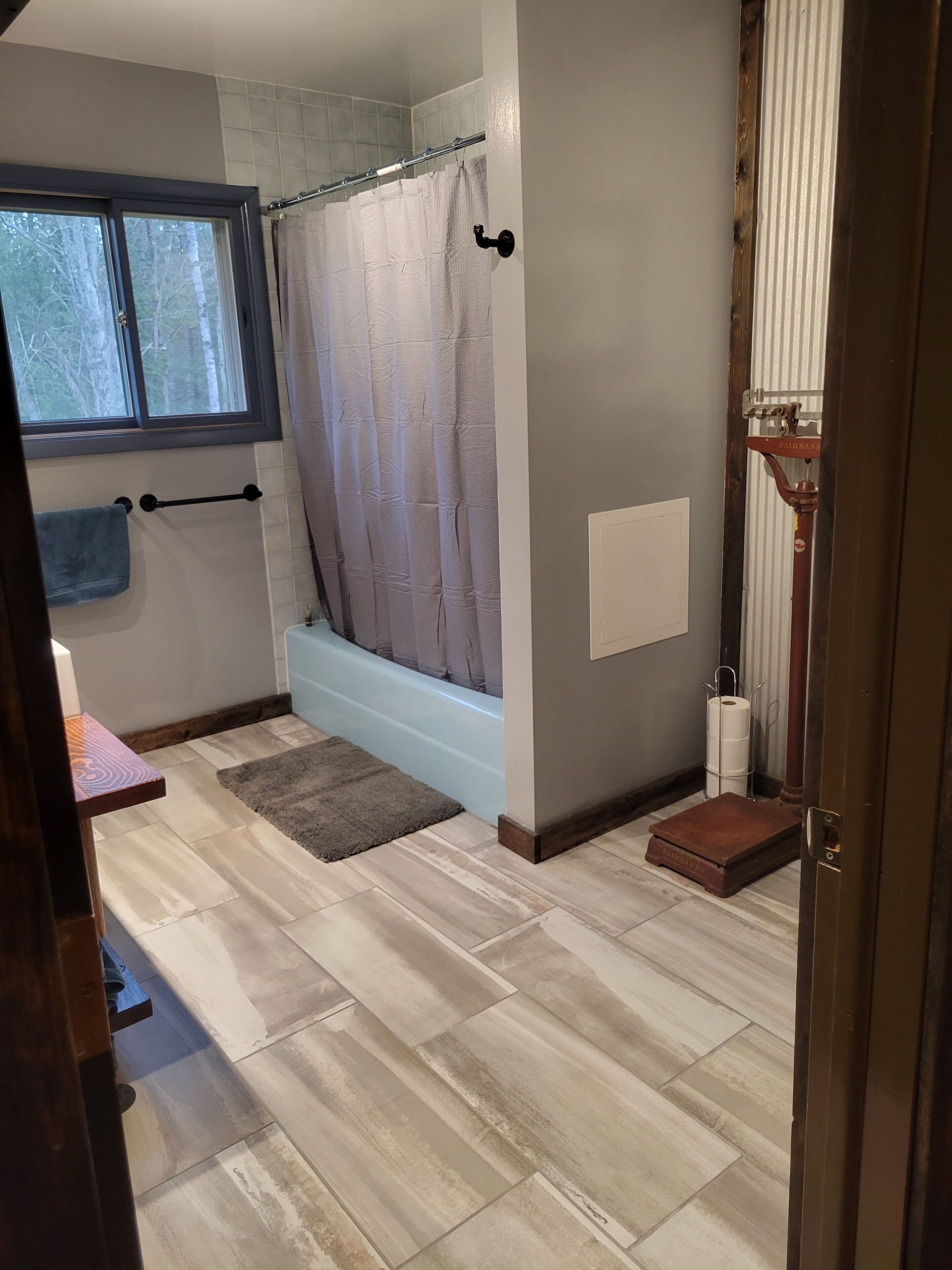 Un baño con bañera, una ventana, toallero, cortina de ducha y dispensador de papel higiénico.