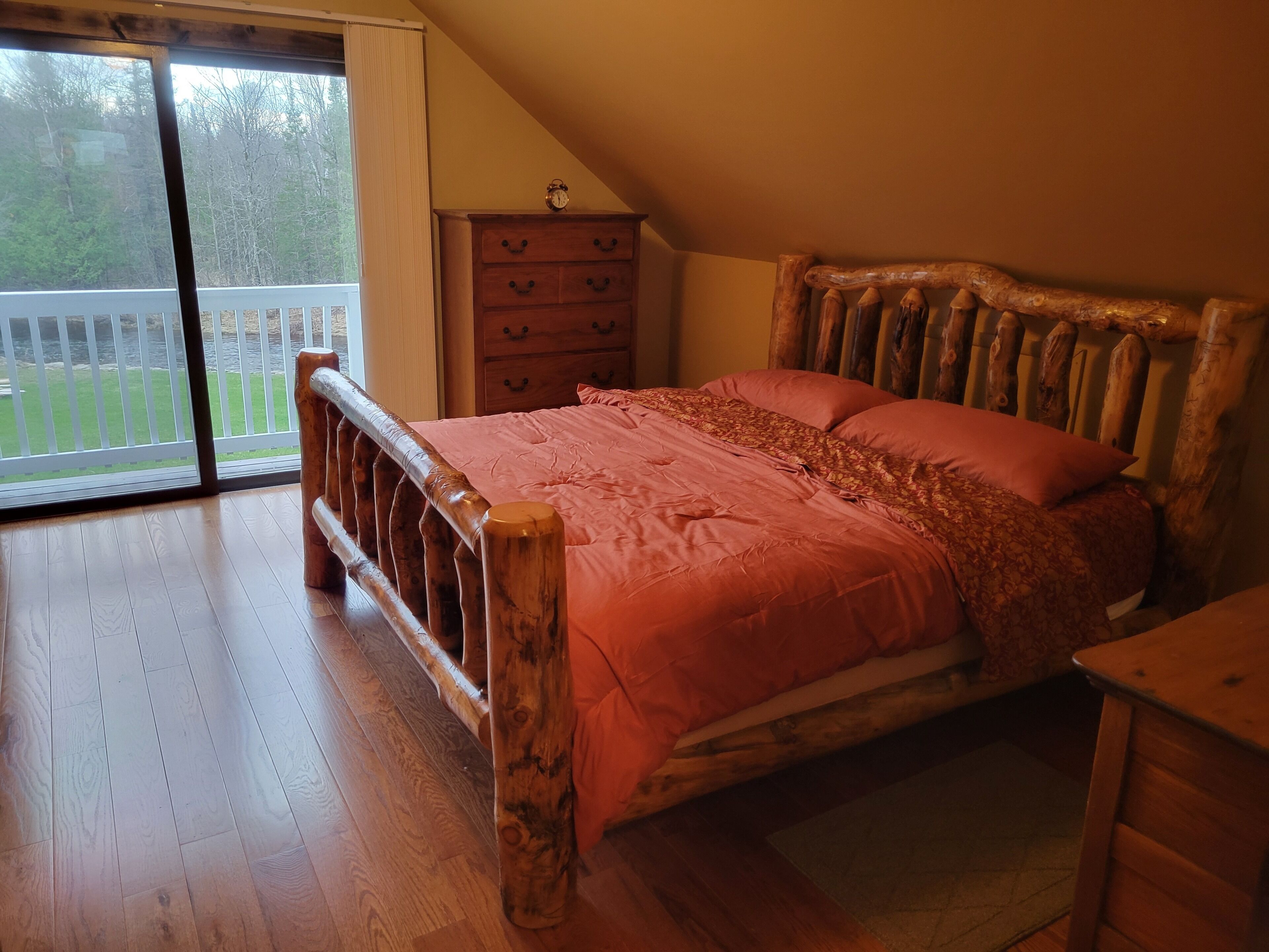 A bedroom with a wooden bed, a dresser, and a view of a balcony.