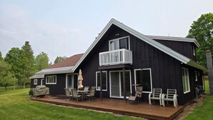 A two-story black house with a balcony, a deck with outdoor furniture, and a lawn.