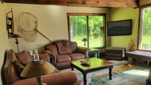 Un salón acogedor con sofá, mesa de centro, televisor y ventana grande con vistas a árboles.