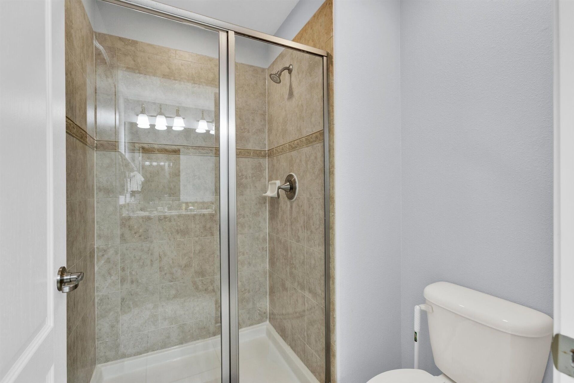 A bathroom with a glass shower enclosure, a toilet, and a sink with a mirror.