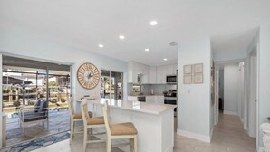 A modern kitchen with a central island, bar stools, and a large clock on the wall. - 🌊 Waterfront Escape | Canal-Front Retreat w/ Private Pool (Naples)