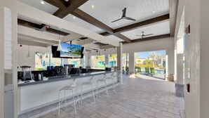 Espaçosa área de bar ao ar livre com vista para a piscina, com design moderno, banquetas brancas e ventiladores de teto.