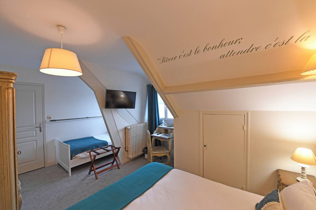 A bedroom with a bed, a desk, a chair, a television, and a wall with a quote.