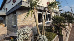 A two-story hotel with a stone facade, balconies with potted plants, and a wooden deck with shrubs. - LA VILLA JULIA (Agon-Coutainville)