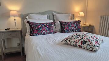 Un lit bien fait, avec du linge de lit blanc et des coussins décoratifs, une table de chevet avec une lampe et un téléphone.