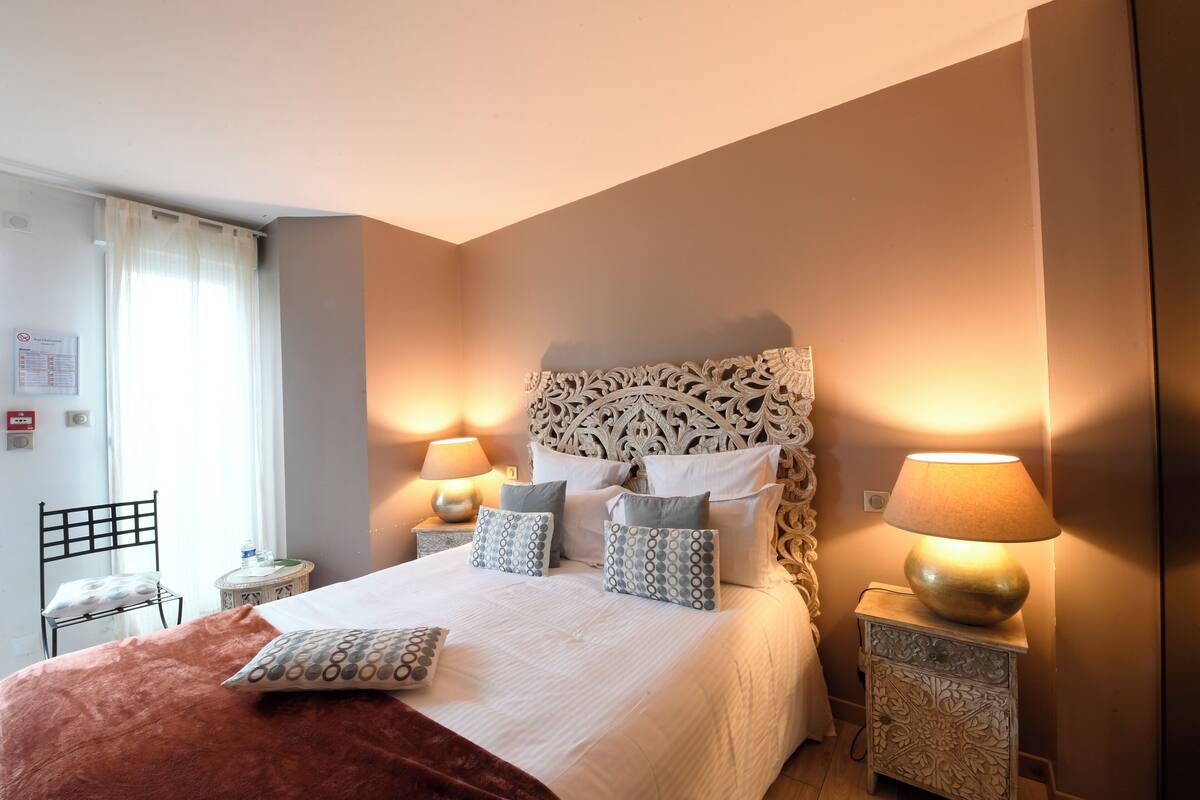 A neatly made bed with a patterned headboard, two bedside lamps, and a chair with a cushion.