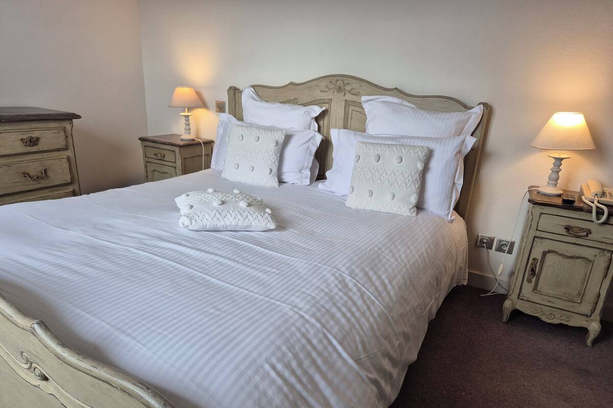 A neatly made bed with white linens and decorative pillows, a wooden headboard, and bedside tables with lamps and a telephone.