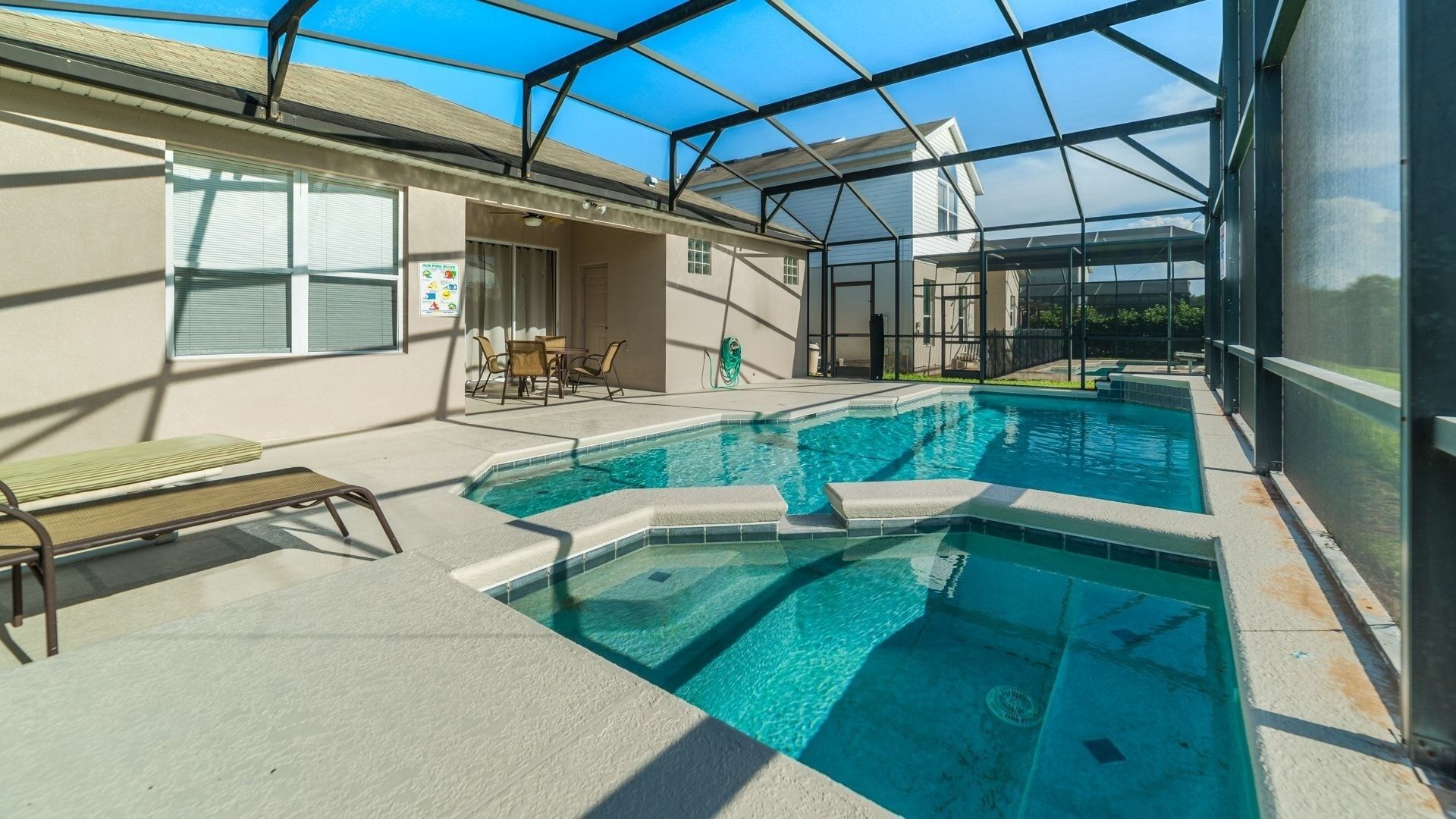 A swimming pool with a glass enclosure, a bench, and a table with chairs.